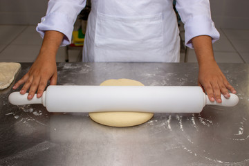 Chef hands rolling the dough with the rolling pin. Making puff pastry on a stainless steal table. First step, dough and the butter on the table.Close up. pastry chef. how to make.