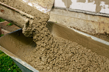 Workmen team in the process of forming foundation blind area. Concrete works with mixer truck and people with wheelbarrow. Labour builders at construction site filling formwork with  cement and gravel