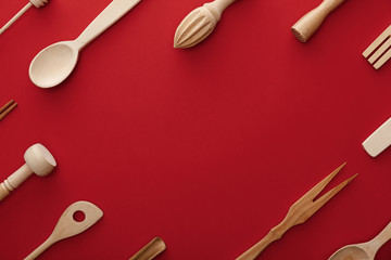 top view of natural wooden spoons, fork and kitchenware on red background with copy space