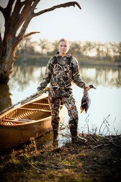 Portrait of a young adult woman duck shooting by a lake.