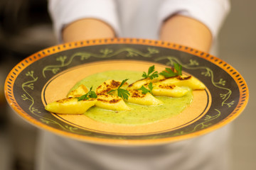 Chef holding a plate with homemade potato gnocchi with blue cheese sauce. focus in the plate. showing just the arms.