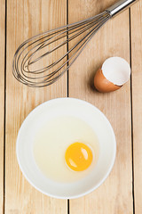 TOP VIEW OF YELLOW EGG IN PLATE NEXT TO SHELLS AND BEATER ON WOOD BACKGROUND