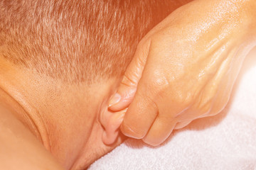 Female professional massage therapist makes therapeutic therapeutic massage of the ears with the hands of a male athlete. woman massages a man