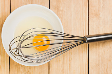 TOP VIEW OF YELLOW EGG IN PLATE NEXT TO SHELLS AND BEATER ON WOOD BACKGROUND