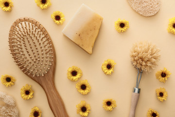 top view of hairbrush, body brush, loofah and piece of soap on beige background with flowers