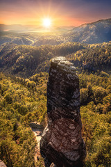 Orange sunset with Sandstonetower and wooded, foggy mountains in the background in Bohemian Switzerland in the Czech Republic - Europe