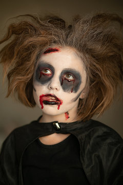 A child in a carnival costume with a scary face painting on Halloween. Black background.