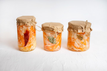 three jars of sauerkraut and carrots in its own juice with spices, white wooden table. traditional home-made, fermented dish of Russia and Germany.
