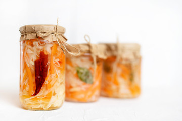 three jars of sauerkraut and carrots in its own juice with spices, white wooden table. traditional home-made, fermented dish of Russia and Germany.