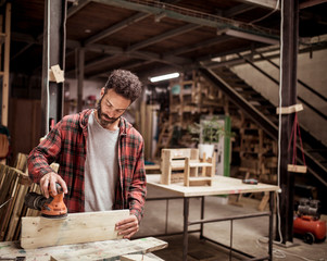 Male carpenter sanding wood while working in workshop