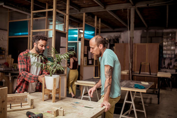 Male carpenters discussing over wooden plant pot holder at workbench