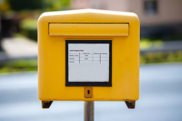A traditional yellow mailbox at a street in Germany. In the middle, the times are indicated when a...