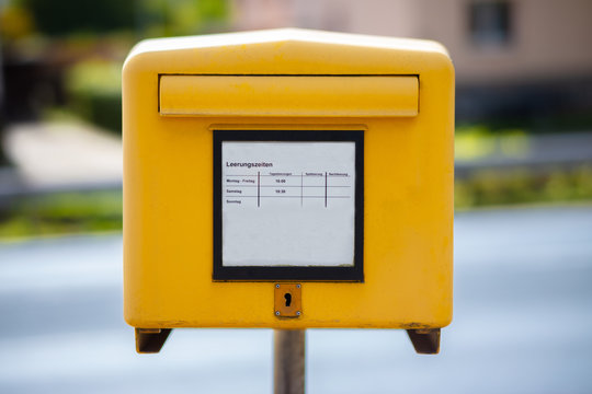 A traditional yellow mailbox at a street in Germany. In the middle, the times are indicated when a discharge takes place. The background is out of focus with nice bokeh.