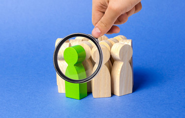 A magnifying glass looks at a green man stands in a crowd of people. Society, social group....