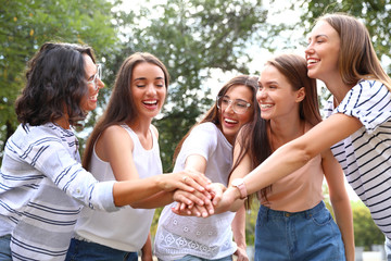 Happy women putting hands together outdoors on sunny day. Girl power concept