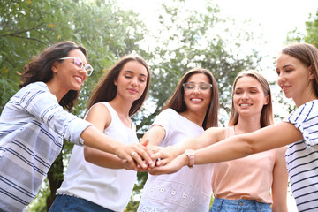 Happy women putting hands together outdoors on sunny day. Girl power concept