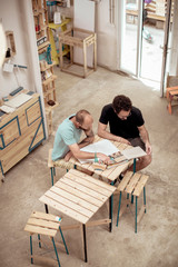 High angle view of male carpenters drawing on paper looking in magazine at desk in office