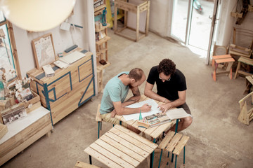 High angle view of male carpenters drawing on paper while sitting at desk in office