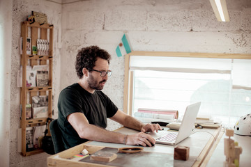 Male carpenter working on laptop at desk by window in office