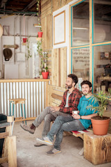 Full length of smiling male colleagues sitting on bench in workshop