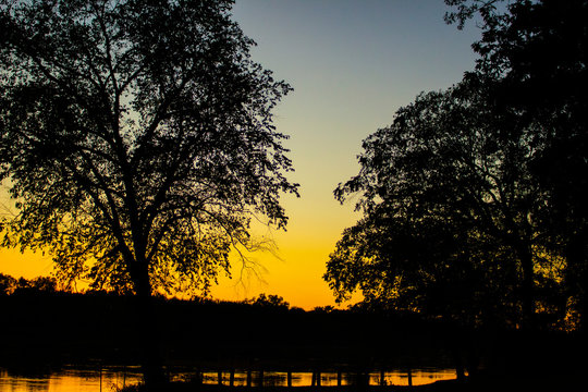 Vibrant Orange Sunset At Boat Landing On Wisconsin River With Silhouette  Trees  