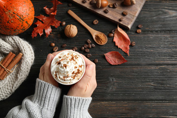 Woman with cup of tasty pumpkin spice latte at black wooden table, top view