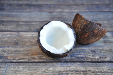 Half a coconut lies on a wooden table. White pulp and coconut shell