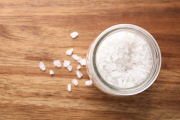 Jar of white sea salt on wooden table, top view with space for text. Spa treatment