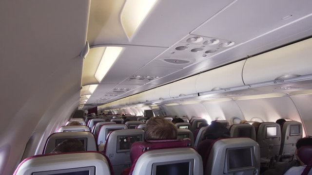 Interior passengers airplane with people on seats. Aircraft cabin with rows of seats. Passengers traveling by a modern commercial plane, inside of an airplane. Travel concept. 4K video.