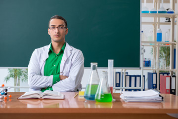 Young male chemist teacher in front of blackboard