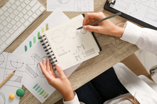 Female designer working at wooden table, top view