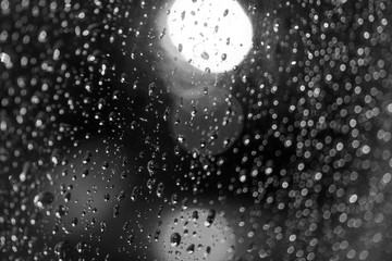 Black and white mood and tone, close up and macro view of raining water drop on glass window and blur background with circle round light bokeh. 