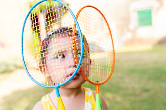 Little girl playing with colorful badminton rackets outdoors in summer