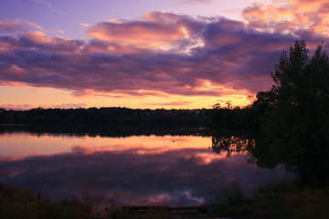 Obraz premium Dramatic sky with cumulonimbus at sunset over the water. Vegetations and foliage in the foreground. Romantic and majestic landscape at countryside. 
