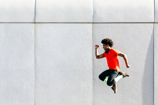 Young man doing jumps with a gray wall in the background