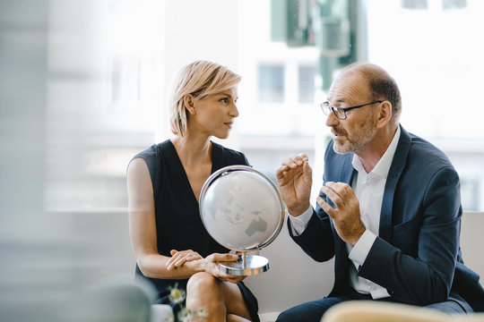 Businessman and woman sitting in coffee shop, looking at globe, discussing business