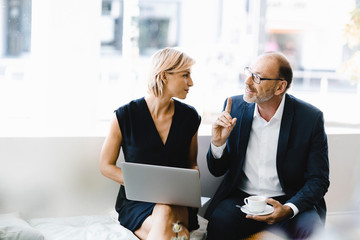 Businessman and woman sitting in coffee shop, using laptop
