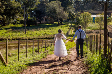 Wedding couple back to back walking on country road.