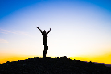 Silhouette of a happy young girl on top of a mountain holding up hands. against the sunset. Success, achievement concept. outdoors