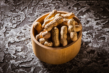 Dried peanuts or nuts on wooden background.Boiled peanuts (amendoim cozido, sergipe, nordeste, Brazil) in a black and yellow bowl and boiled peanuts spread and open outside the bowl. - obrazy, fototapety, plakaty