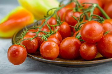 Close up view of red cherry tomatoes bunch in a plate and yellow sweet pepper on light background