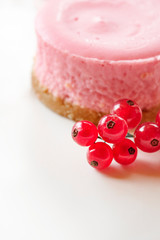 Pink round strawberry or raspberry cheesecake decorated with a bunch of red currants