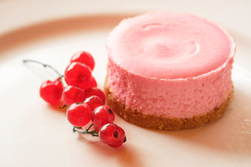 Pink round strawberry or raspberry cheesecake decorated with a bunch of red currants