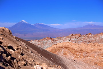 Atacama desert, Chile. Colorful hills and valleys with dry soil and dusty trail. Mountains in the background and blue sky