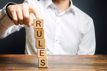 A man holds a tower of blocks with the word Rules from falling. Setting clear rule and...