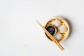 Traditional chinese steamed dumplings Dim Sums in bamboo steamer with sauces and chopsticks on light surface with copy space. Asian food background. - obrazy, fototapety, plakaty