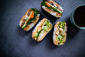 Tempeh, carrot and spinach onigirazu with broccoli, cashew and coriander onigirazu on concrete background. Food from Japan. Top view.