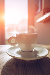 Hot Cappuccino coffee on the table with blurry kitchen background with sun flare, vintage tone