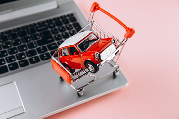 Black friday concept. Red trolley with car near laptop on pink background