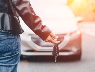 Woman holding a car keys. Blurry car in background.